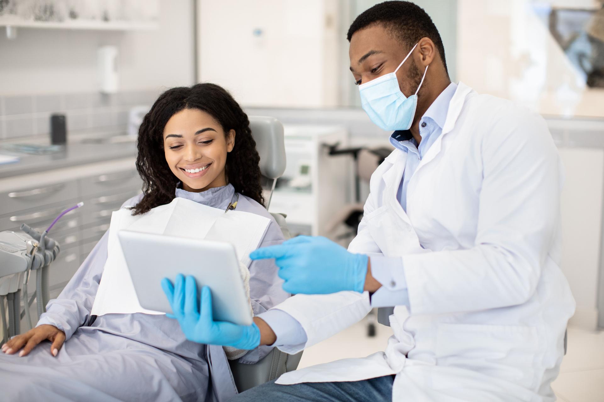 Black Dentist Doctor With Digital Tablet Consulting Female Patient In Modern Clinic